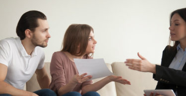 Letting agent has a discussion with two tenants, a young man and a young woman, on a sofa