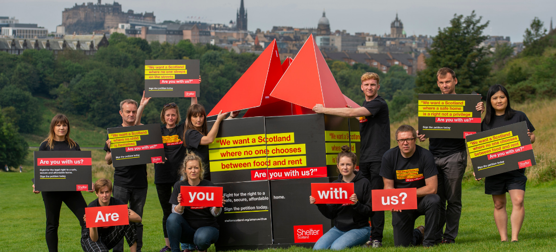 Shelter Scotland campaigners with a large house prop and signs that say "Are you with us?"