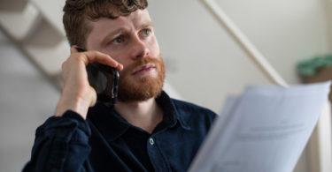 Young man looking worried on the phone, holding some forms
